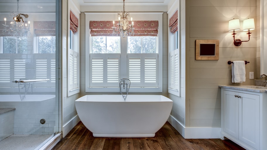 Primary bathroom with a large standalone tub, crystal chandelier, shiplap walls, hardwood floors, and large glass shower door